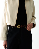 A cropped off-white jacket with brown collar panels, worn over a black top and black wide-leg jeans with a brown belt, shown on a model against a white studio background.
