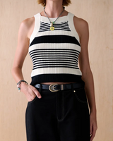 A model wearing a black and white horizontally striped ribbed knit halter crop top, paired with black wide-leg jeans, a black belt, and layered necklaces, standing against a light wood panel background.